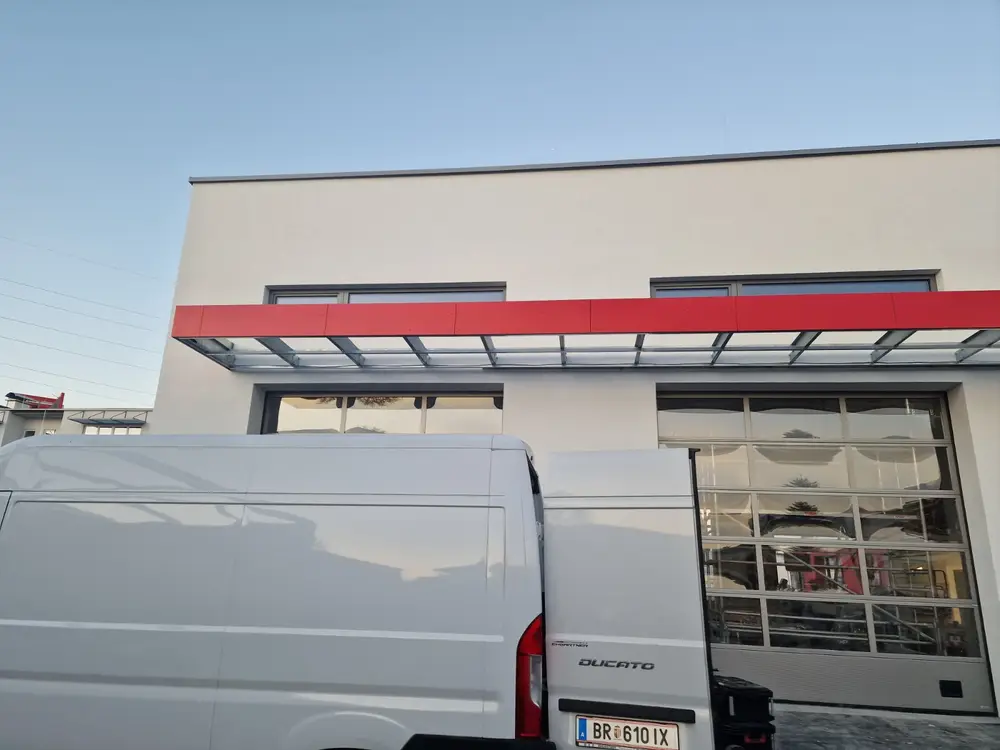 Glasvordach auf Stahlkonsolen über den Toren einer Gewerbehalle, davor ein Kastenwagen