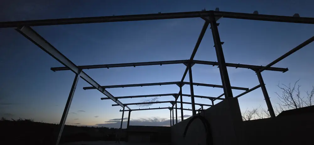 Dieselbe Carport-Konstruktion in der Dämmerung, Rahmen und Sparren als Silhouette gegen den Abendhimmel