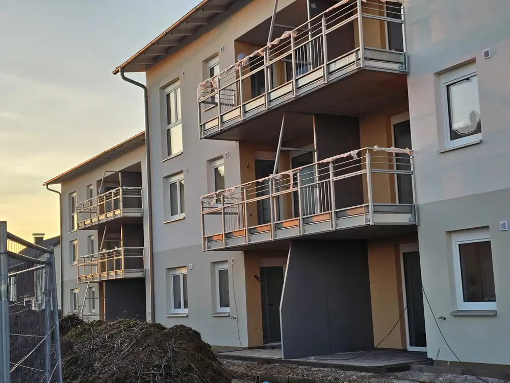 Wohnanlage im Abendlicht, an jeder Loggia eine Edelstahlbrüstung mit waagrechten Holmen, Geländer noch eingepackt