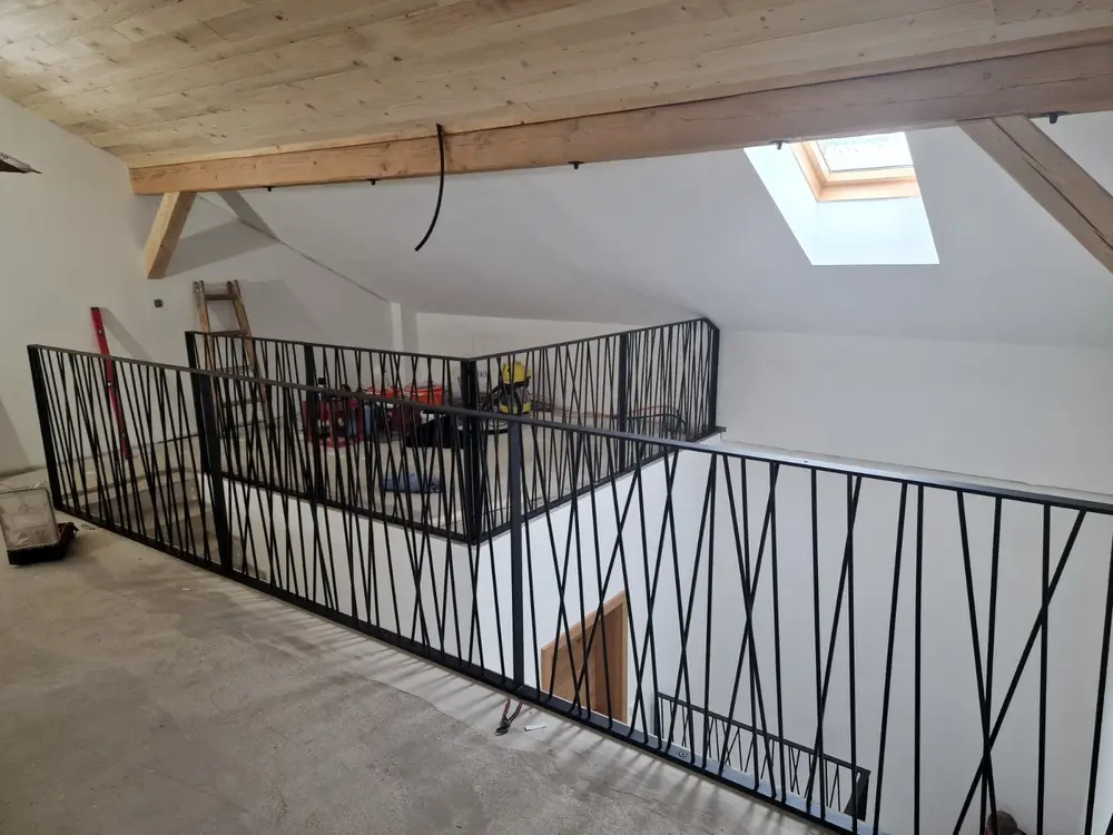 Galeriegeländer aus schwarzem Stahl mit Zickzack-Füllung, Blick entlang der Brüstung unter dem Dachstuhl