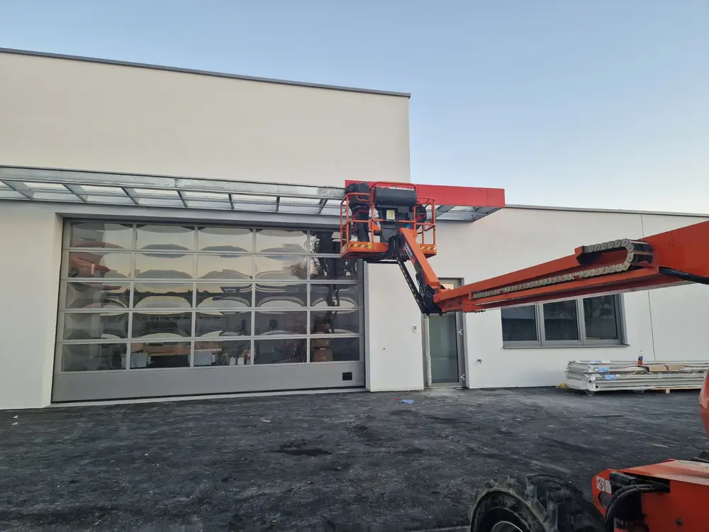 Gewerbehalle mit Glasvordach über dem Sektionaltor, daneben eine Hubarbeitsbühne bei der Montage
