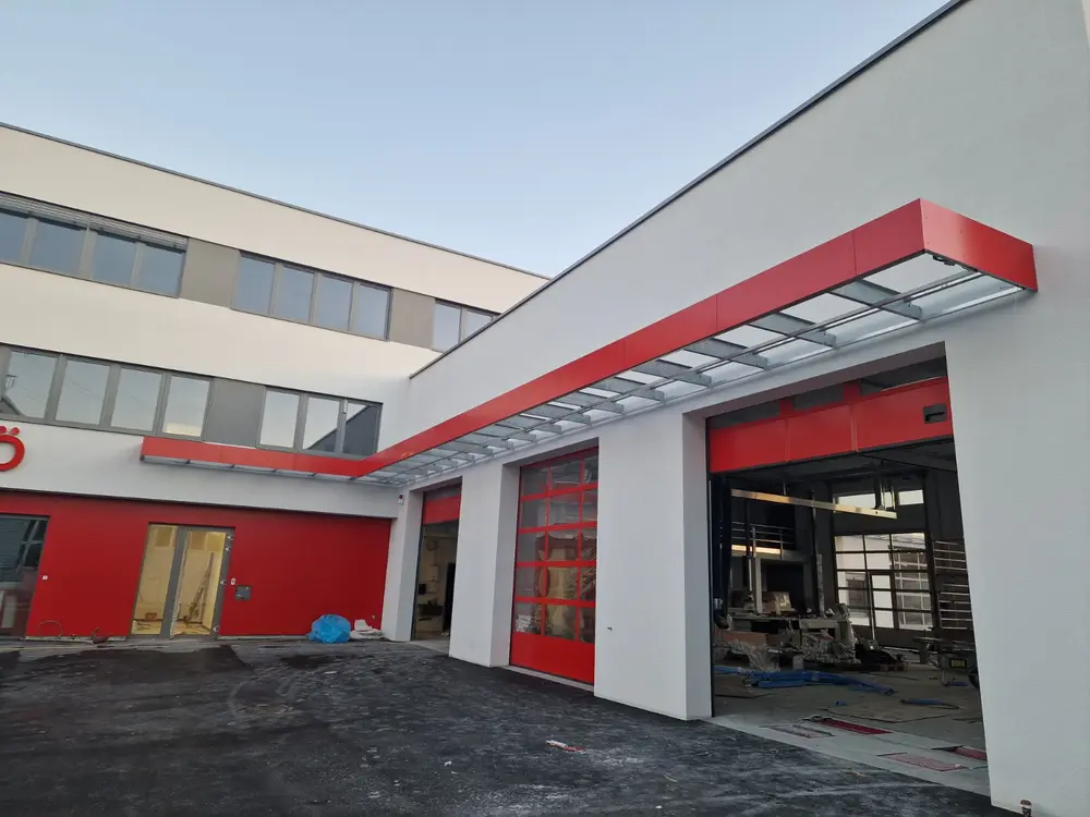 Gewerbebau mit umlaufendem Vordach aus Stahl über den roten Hallentoren