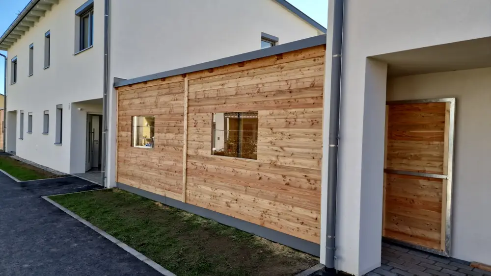 Holzverkleidete Wand in einem umlaufenden Stahlrahmen zwischen zwei Gebäudeteilen