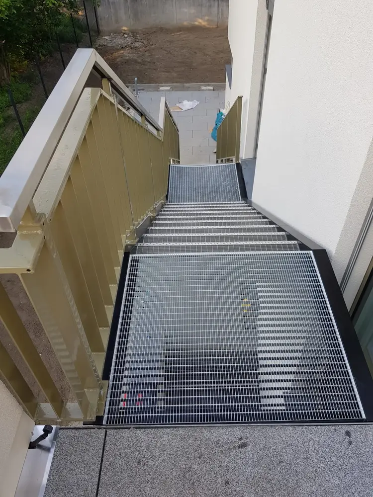 Außentreppe mit Antrittspodest aus Gitterrost, von oben zwischen Hauswand und Wange gesehen