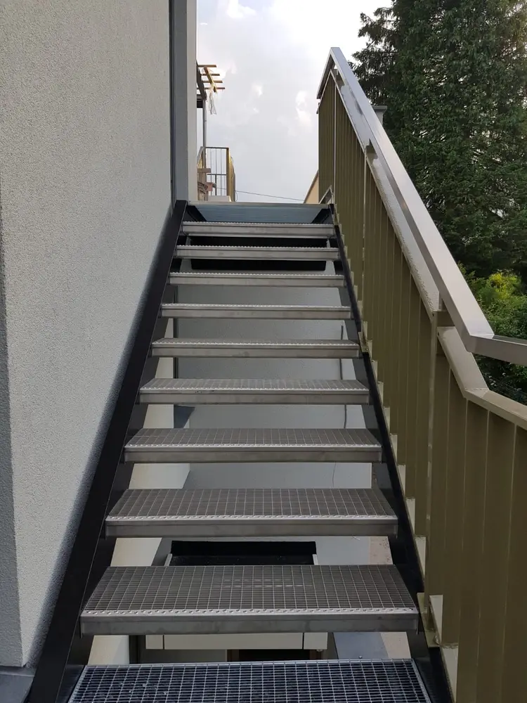 Außentreppe zwischen Hauswand und Sichtschutzwand, Gitterroststufen auf einer Stahlwange
